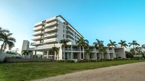 A multi-story hotel with a modern design, featuring balconies and a well-maintained lawn. - Oceanfront 2BR Condo at Zantamar | Beachfront Pools & Luxury Amenities (La Cruz de Huanacaxtle)