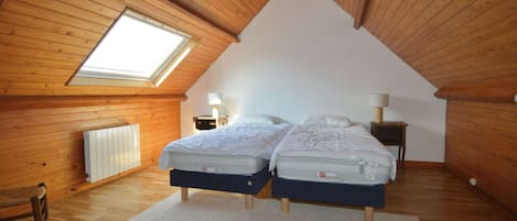 A bedroom with two beds, a skylight, wooden walls, and a radiator.