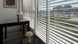Een kamer met een groot raam, een bureau, een stoel en een aan de muur hangend schilderij.