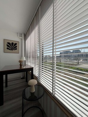A room with a large window, a desk, a chair, and a wall-mounted picture. - Voile du cap, studio with loggia overlooking the port (Courseulles-sur-Mer)