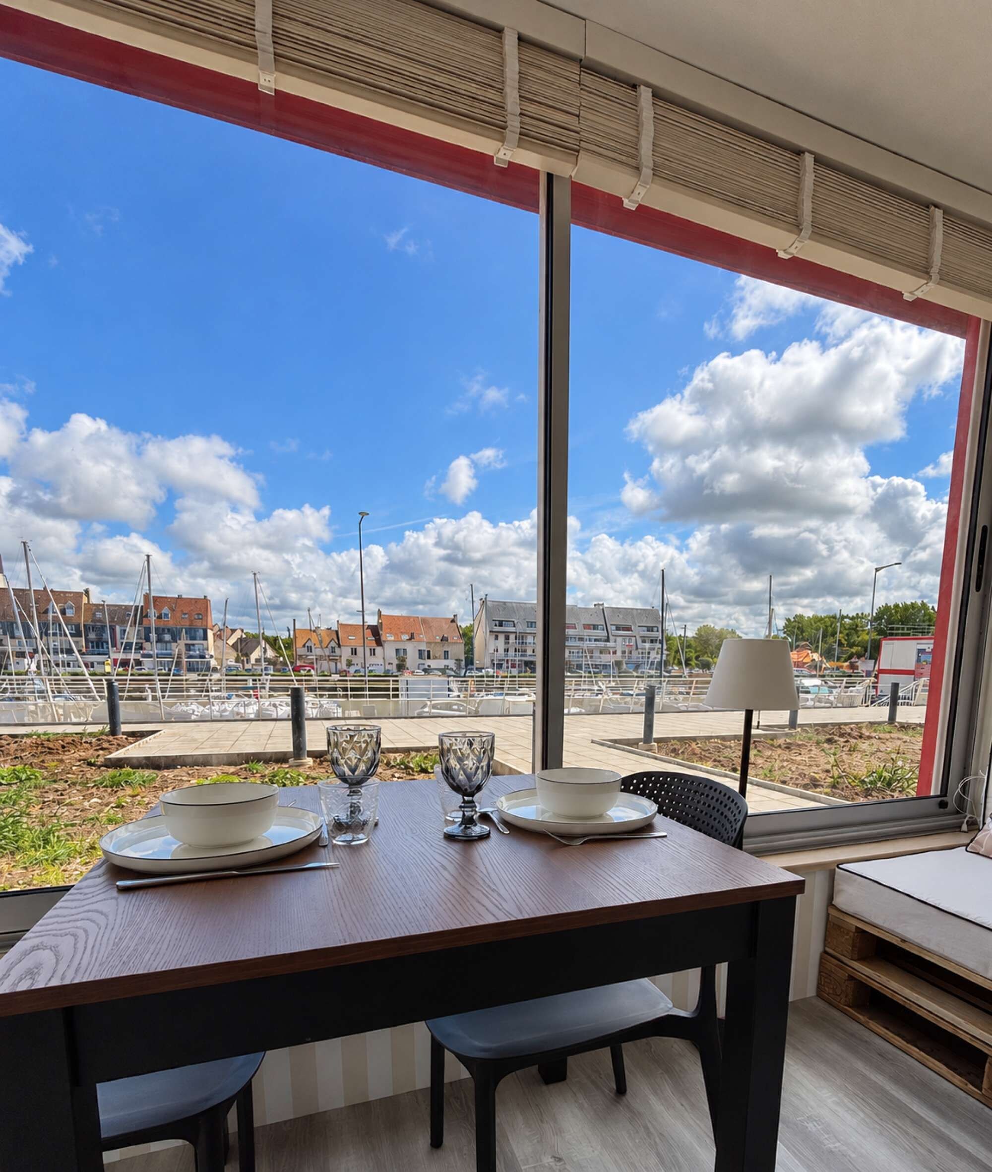 A dining area with a table set for four, large windows offering a view of a marina and buildings.