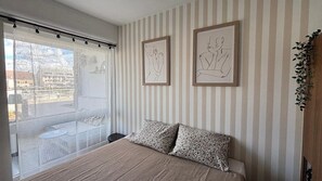 A bedroom with a bed, striped wallpaper, and two framed artworks. - Voile du cap, studio with loggia overlooking the port (Courseulles-sur-Mer)