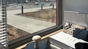 Een kamer met een groot raam, een bank, een tafeltje en een potplant.
