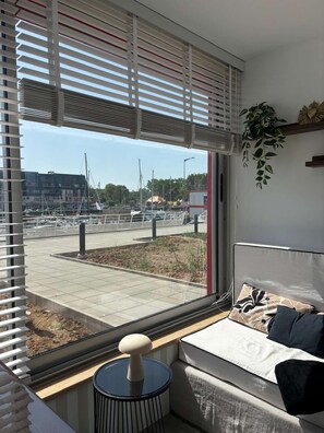 A room with a large window, a sofa, a small table, and a potted plant. - Voile du cap, studio with loggia overlooking the port (Courseulles-sur-Mer)