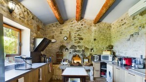 Une cuisine rustique avec des murs en pierre, des poutres en bois, une cheminée en pierre, une table à manger et des appareils électroménagers modernes.