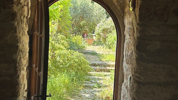 Un portail en arc donne accès à un espace extérieur aménagé en jardin, avec un chemin de pierre et de la verdure.