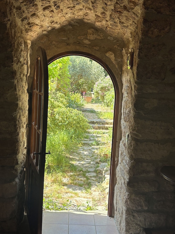 An arched doorway leading to an outdoor garden area with a stone path and greenery. - Charming house in Provence with outbuilding - Swimming pool - 15 people (Aurons)