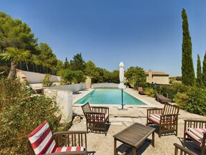 A pool area with chairs and a table, surrounded by greenery and stone walls. - Charming house in Provence with outbuilding - Swimming pool - 15 people (Aurons)