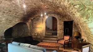 Un intérieur aux murs de pierre, avec un canapé, des fauteuils, une table et une cheminée.