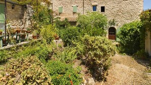 Un bâtiment en pierre doté d’une cour, de plantes en pot et d’un espace extérieur aménagé avec des meubles rustiques.