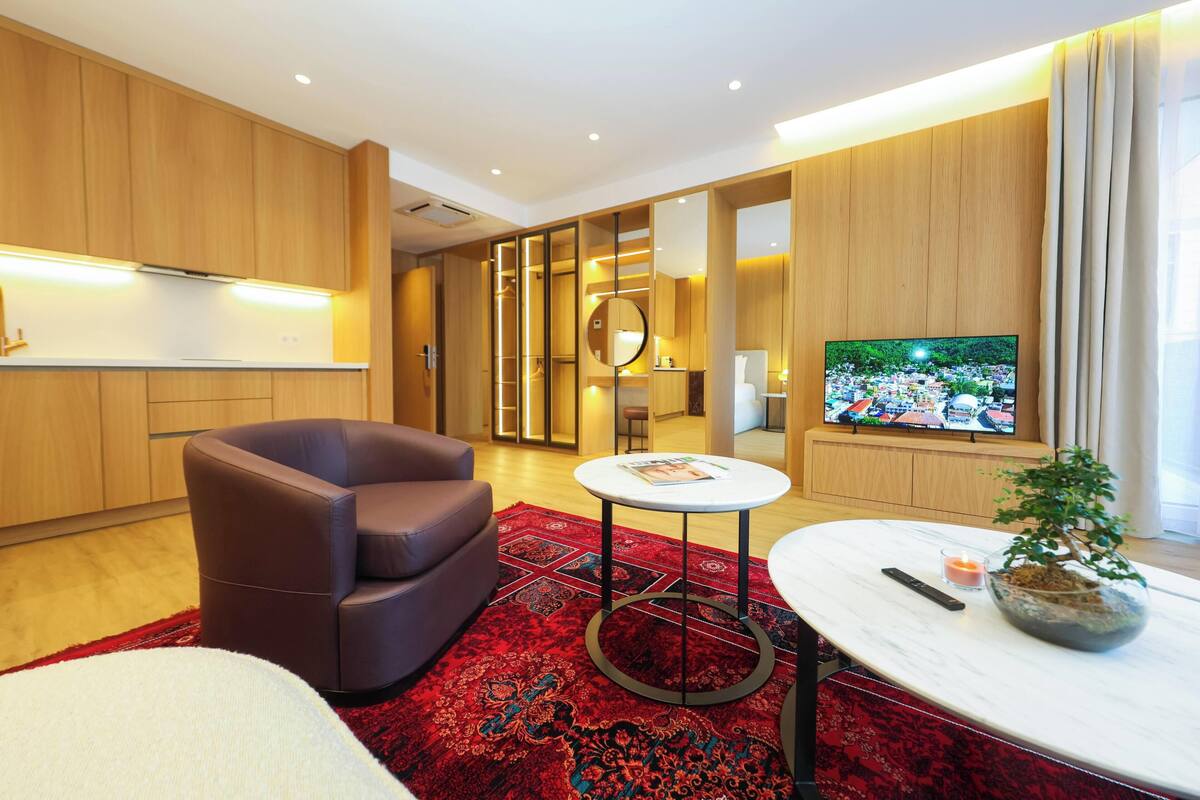 Habitación de hotel moderna con sofá, una mesa redonda, televisión y una pequeña planta.