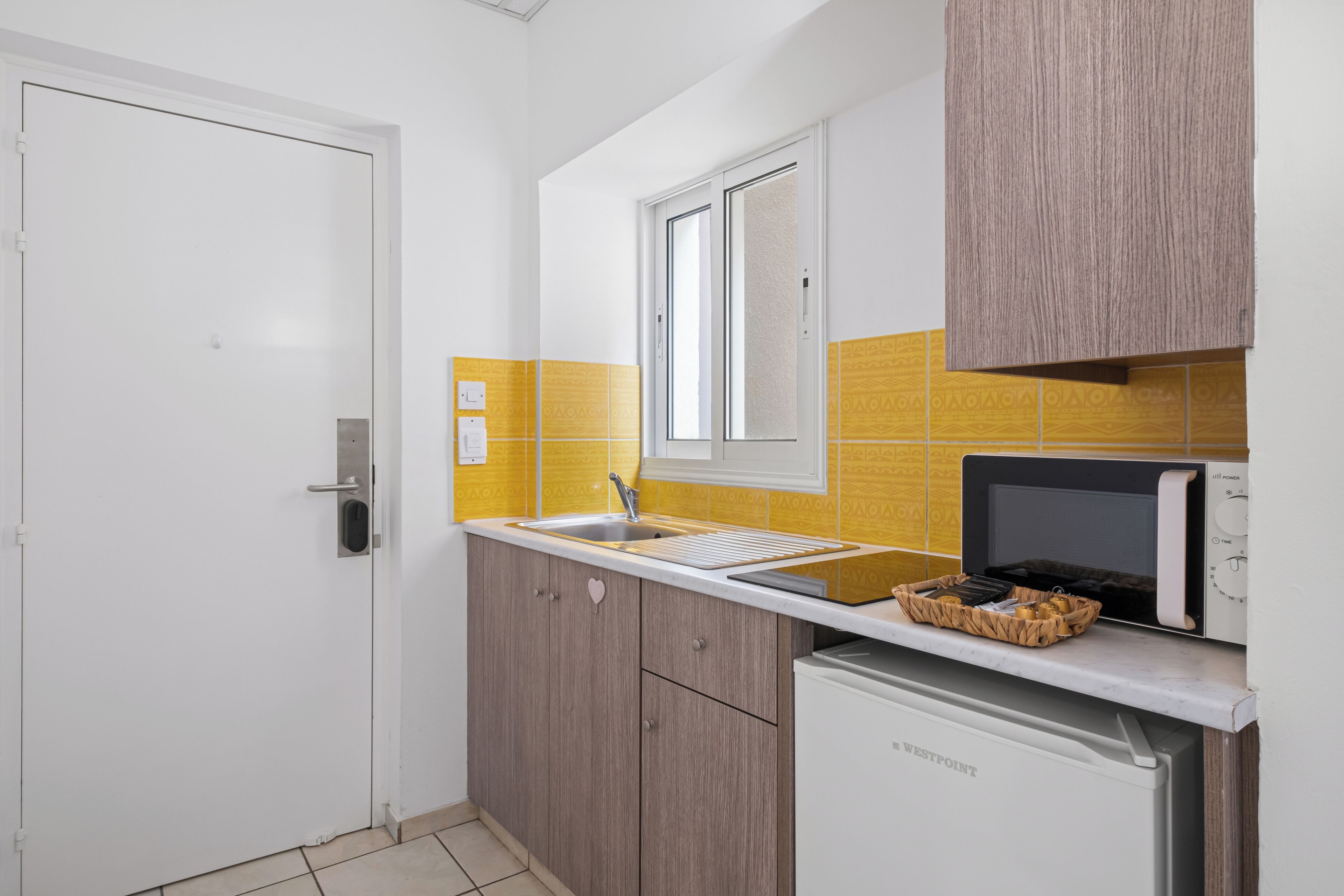 A compact kitchen with a white door, a window, a microwave, and a dishwasher.