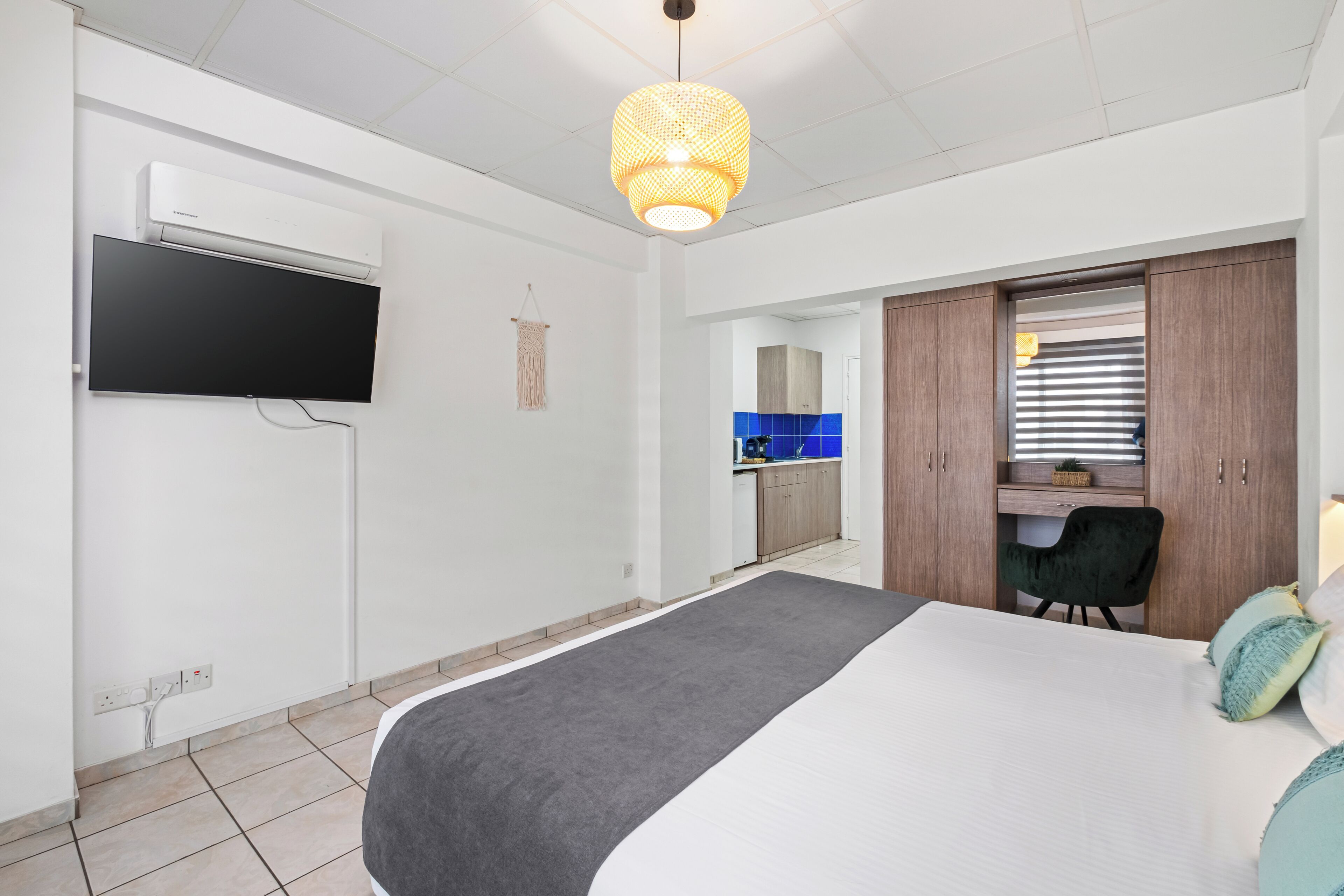 Ein Schlafzimmer mit Bett, einem an der Wand befestigten Fernseher, einem Schreibtisch mit Stuhl und einem Kleiderschrank.