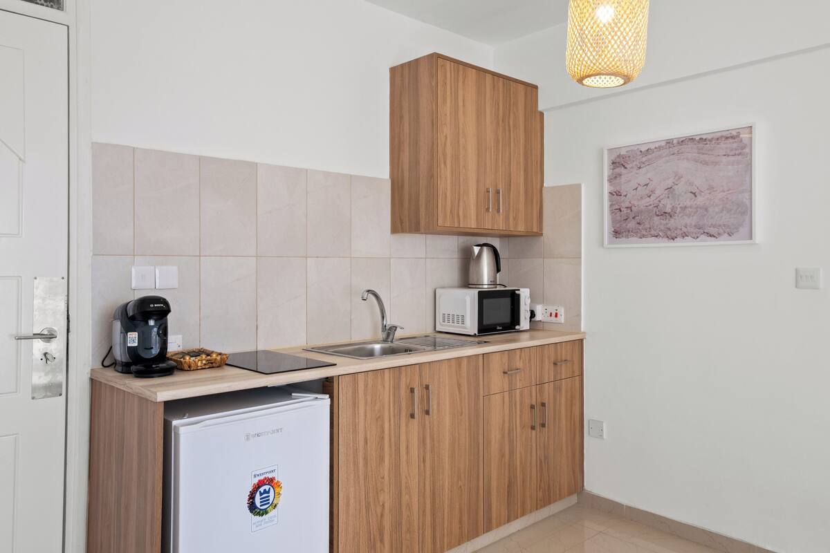 A compact kitchen with a refrigerator, a coffee maker, a microwave, and wooden cabinets.