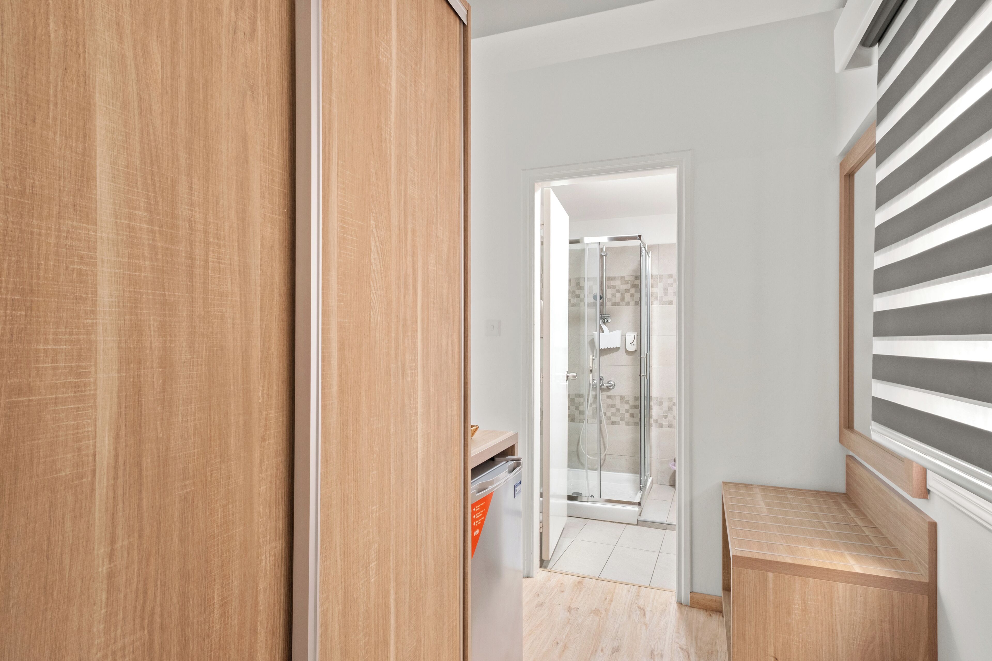 A hallway with a wooden door, a small trash bin, and a shower area with a glass door.