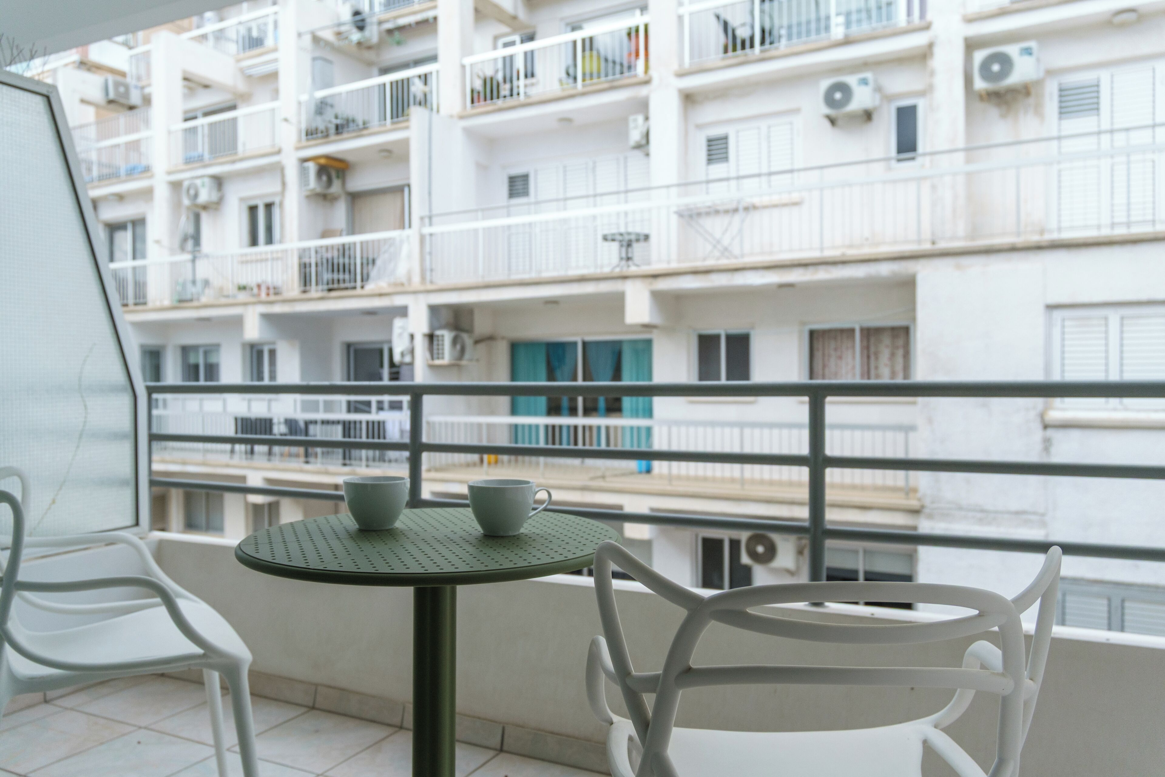 Un balcón con mesa y sillas, con vista a un hilera de edificios de apartamentos blancos.