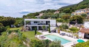 Ein modernes, zweistöckiges Haus mit Schwimmbad, umgeben von üppiger Vegetation und Hügeln.