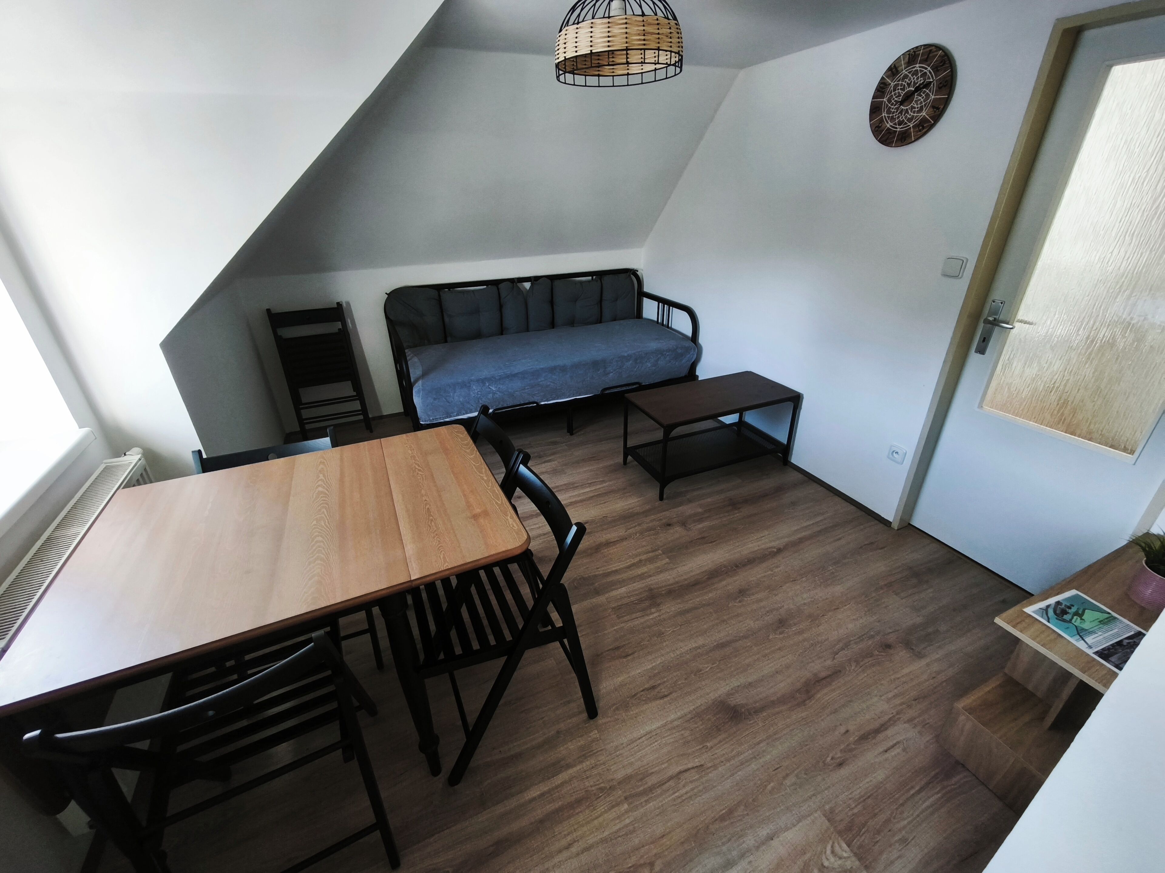 Une pièce de taille modeste comprenant une table à manger, des chaises, un canapé, une petite table, un luminaire suspendu et une porte.