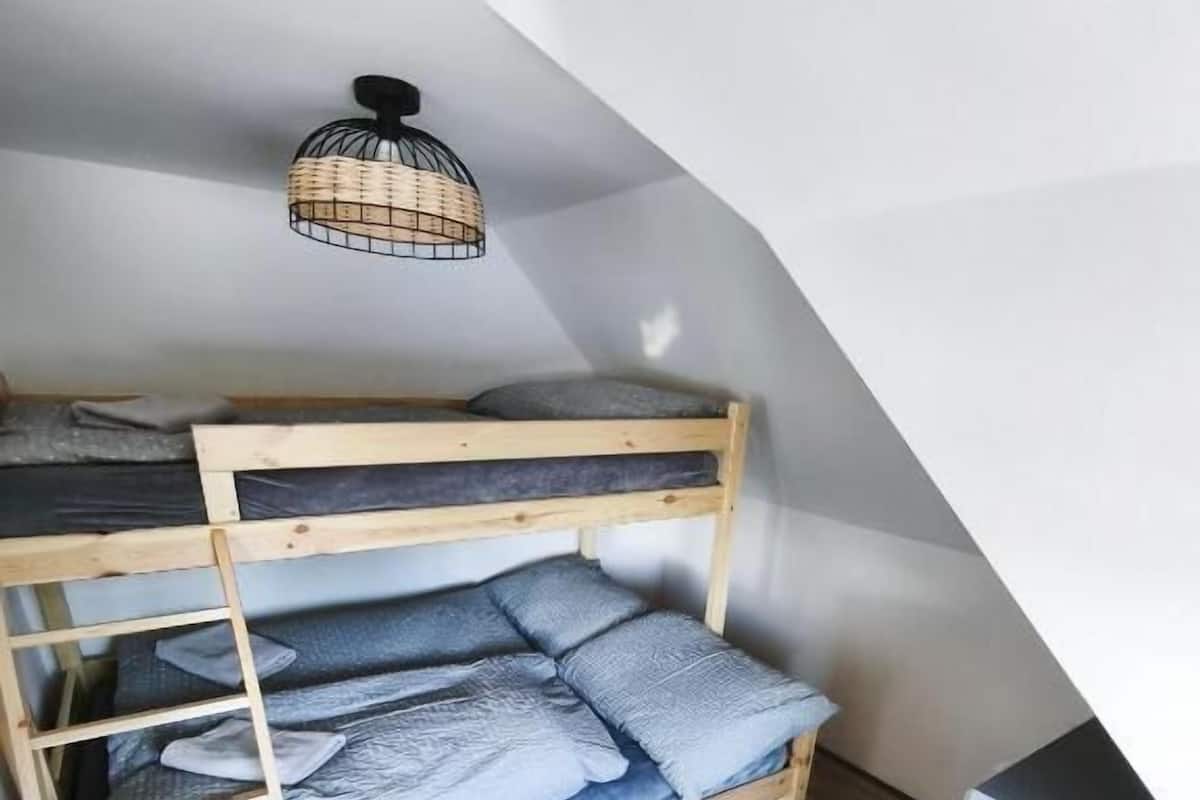 A bunk bed with a ladder, a hanging light fixture, and a wooden floor.
