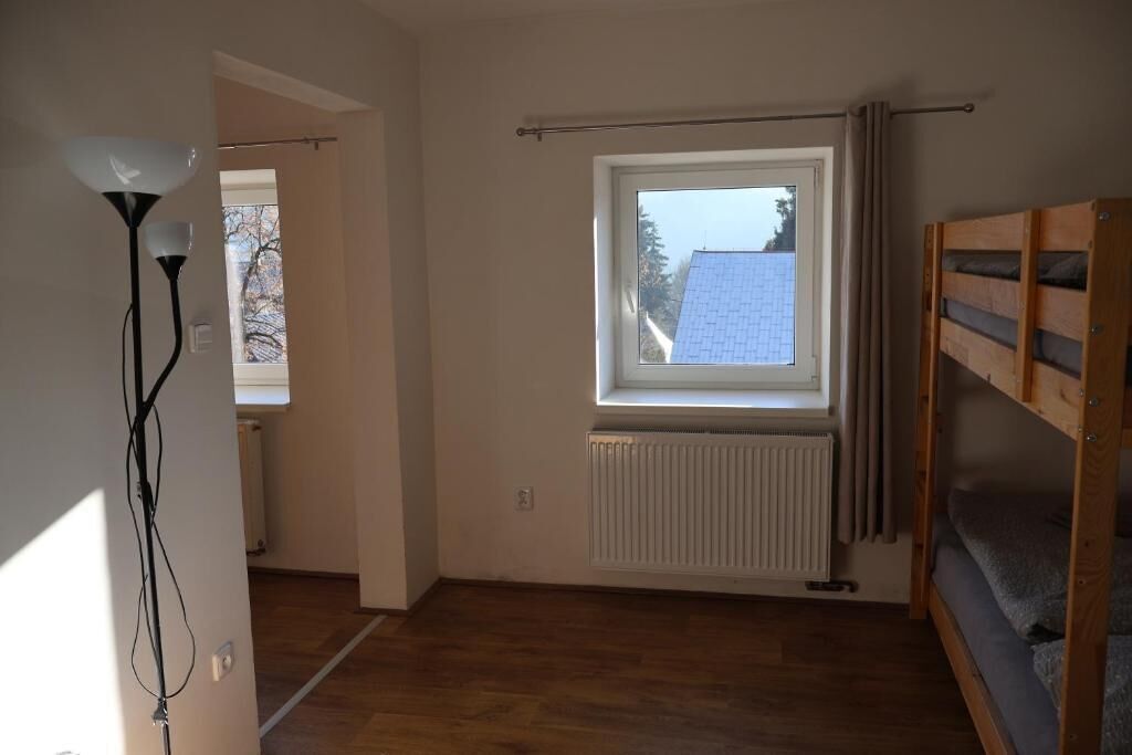 A room with a window, radiator, wooden bunk bed, and a lamp.