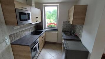 Una cocina compacta con horno integrado, microondas y ventana con vista a la vegetación.