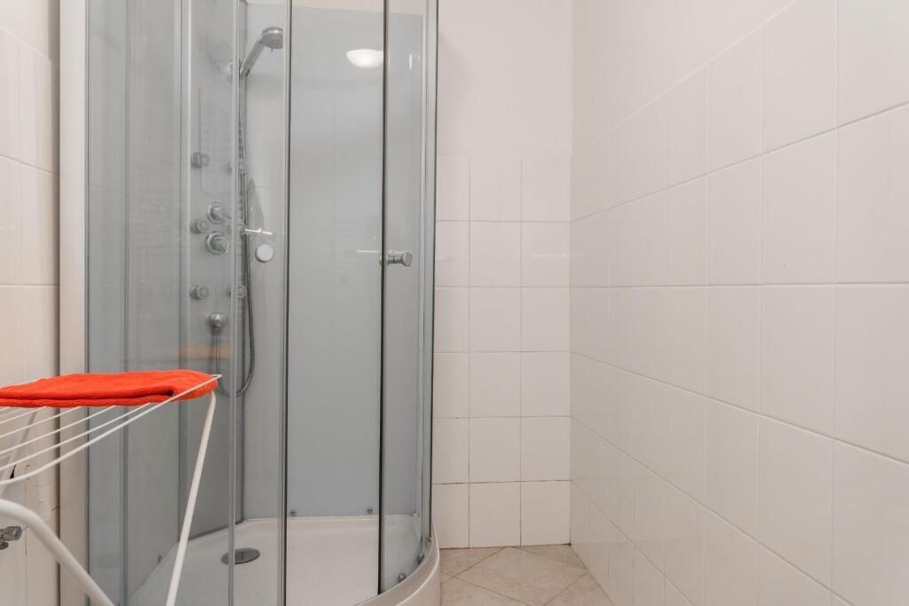 Box de chuveiro com paredes de azulejos brancos, uma toalha vermelha em um suporte e piso branco.