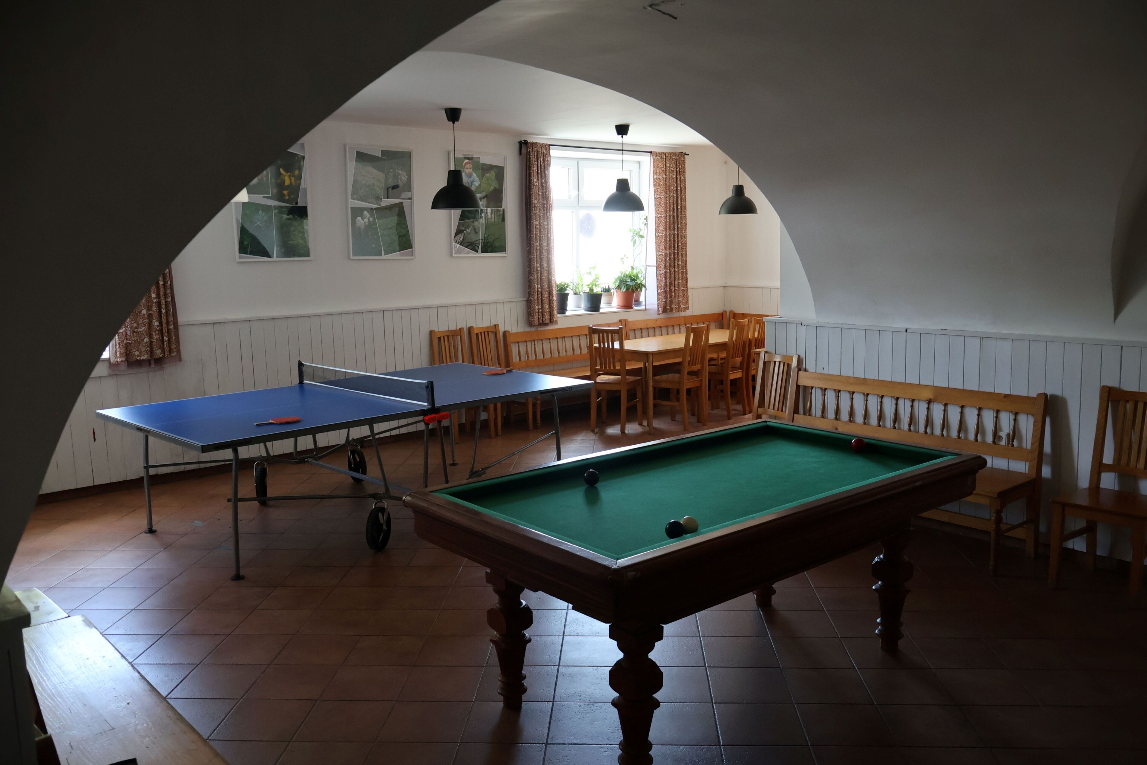 Een biljartruimte met een pooltafel, twee tafeltennistafels en een eethoek met houten stoelen en banken.