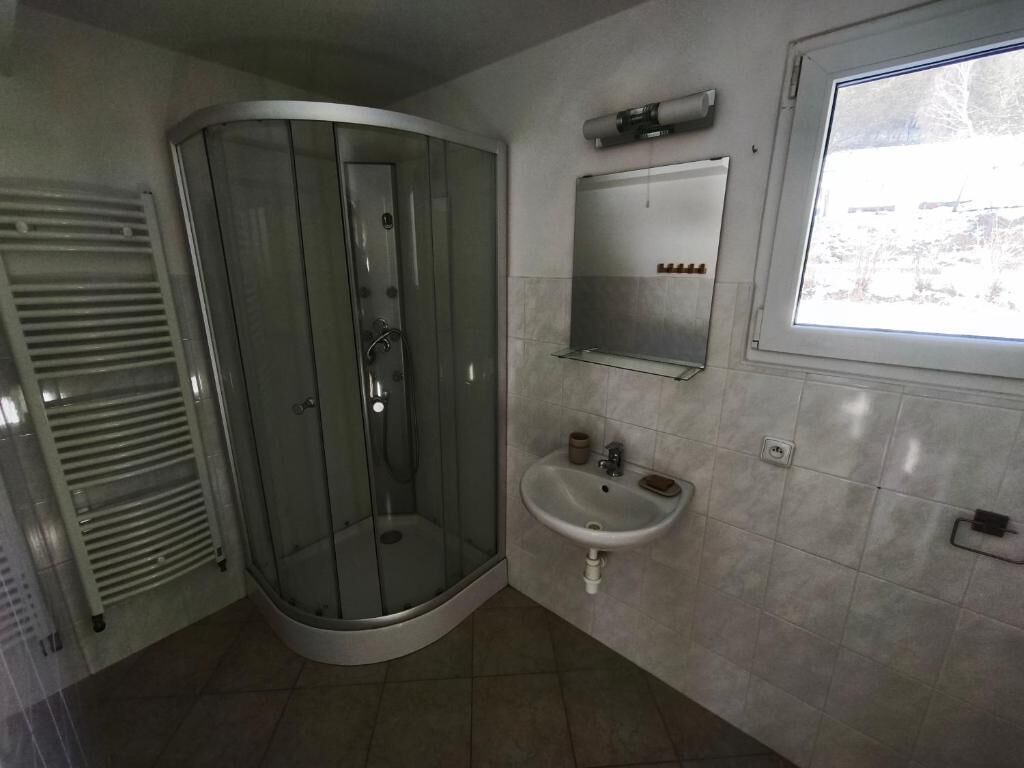 A bathroom with a glass shower enclosure, a sink, a mirror, and a window.