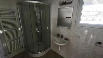 A bathroom with a glass shower enclosure, a sink, a mirror, and a window.