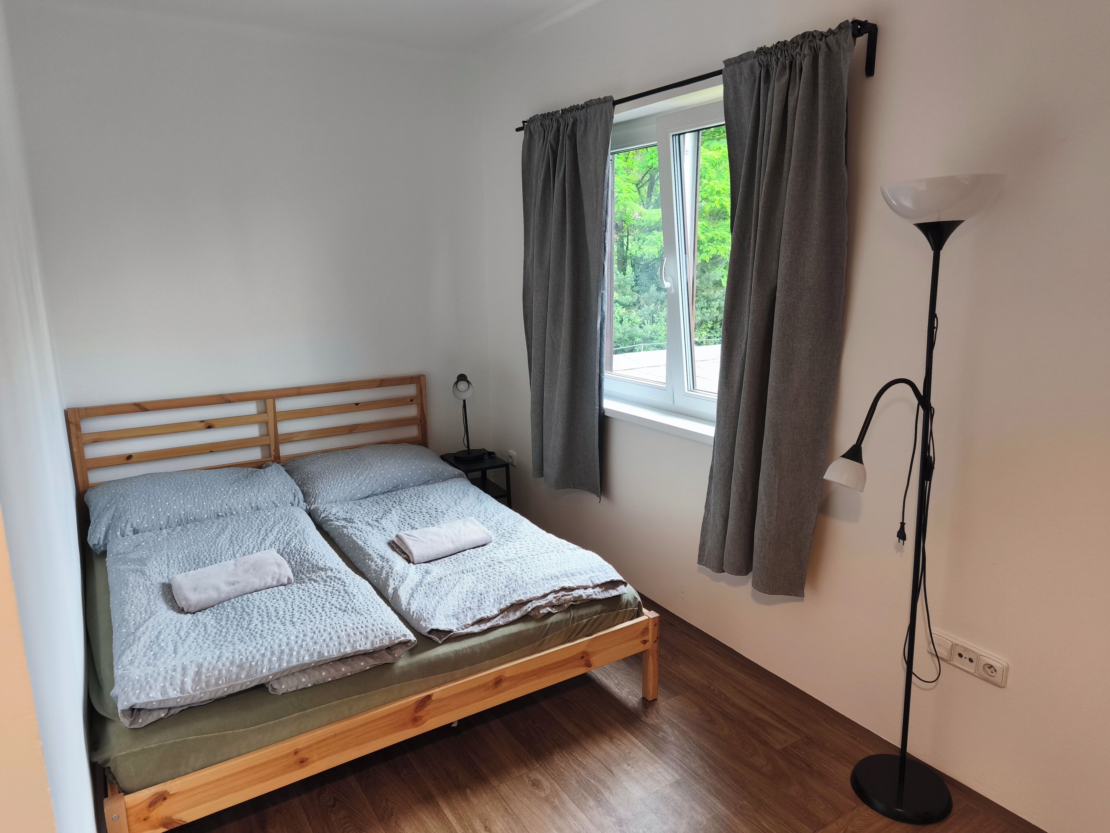 Ein Einzelbett mit Holzrahmen, ein Nachttisch mit Lampe und ein Fenster mit Vorhängen.