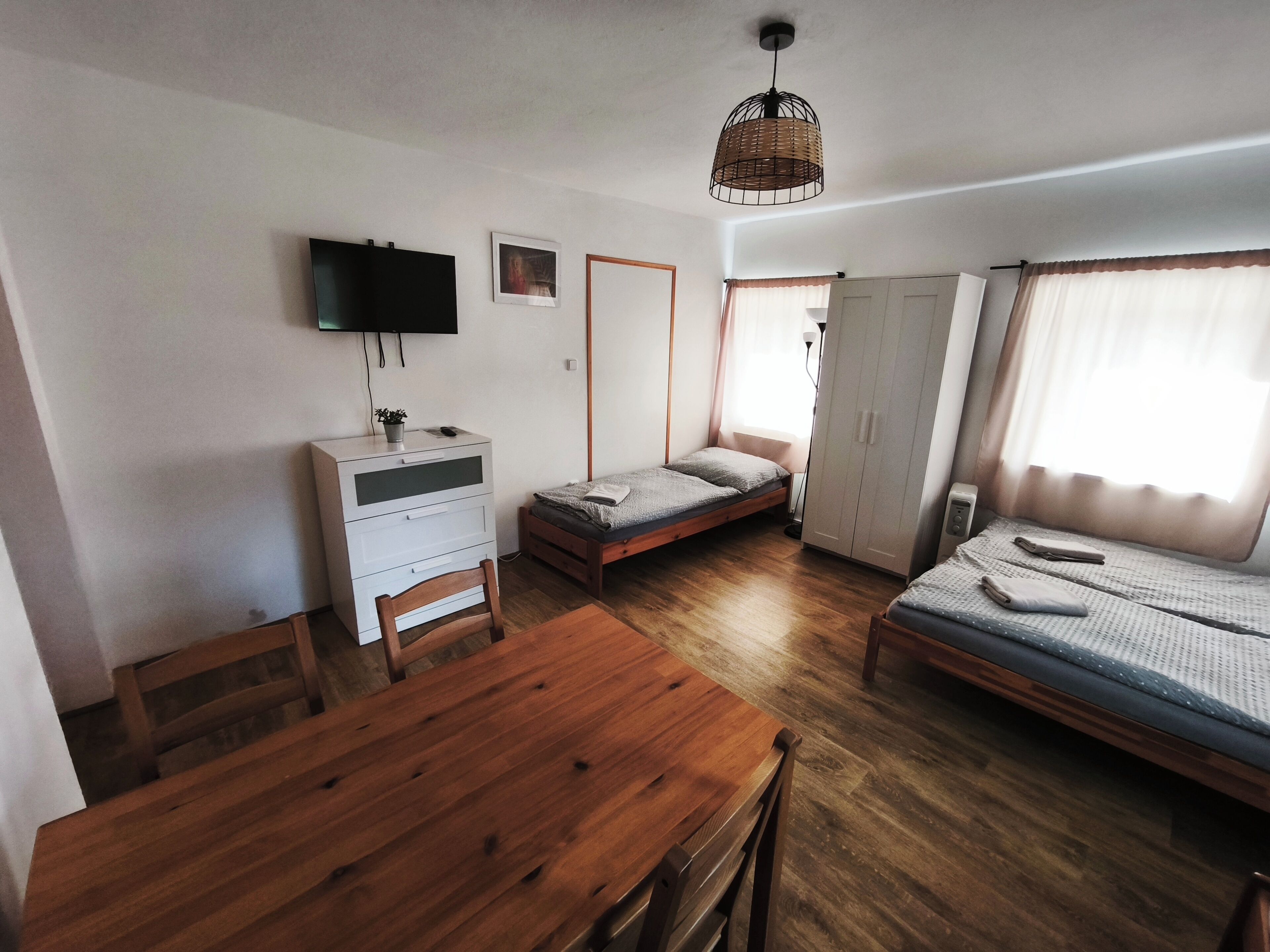 Una habitación compacta con una mesa de comedor de madera, una cama individual, una mesita de noche pequeña, un armario y un televisor montado en la pared.