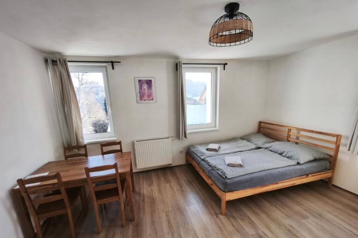 A bedroom with a wooden bed, a wooden table, two windows, and a hanging light fixture.