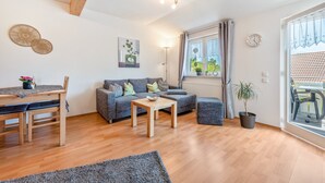 Ein modernes Wohnzimmer mit einem Holzesstisch, einem grauen Sofa und einem großen Fenster mit Vorhängen.