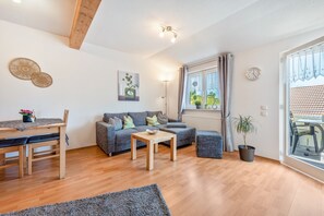 Ein modernes Wohnzimmer mit einem Holzesstisch, einem grauen Sofa und einem großen Fenster mit Vorhängen.