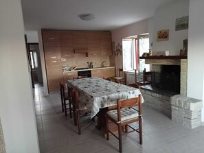 A dining area with a table and chairs, a kitchen in the background, and a fireplace. - THE HOUSE ON THE LAKE - App. WISTERIA - MAIELLA PARK (Abruzzo)