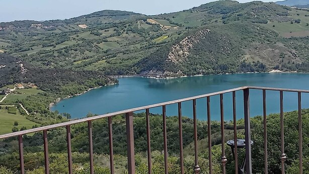 A scenic view of a lake surrounded by green hills, with a metal railing in the foreground. - THE HOUSE ON THE LAKE - App. WISTERIA - MAIELLA PARK (Abruzzo)