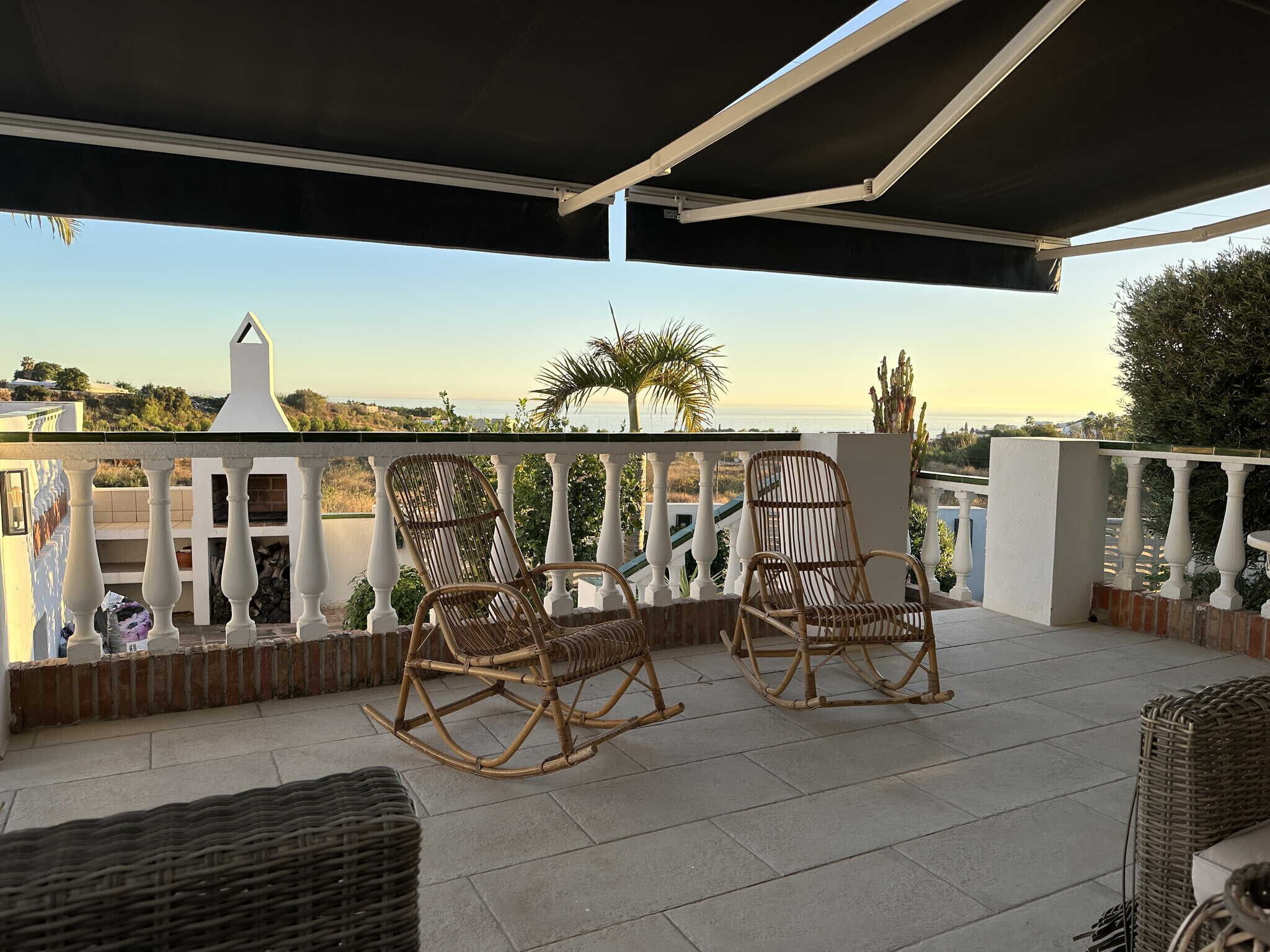 A balcony with two wicker rocking chairs, a white railing, and a view of the sea.