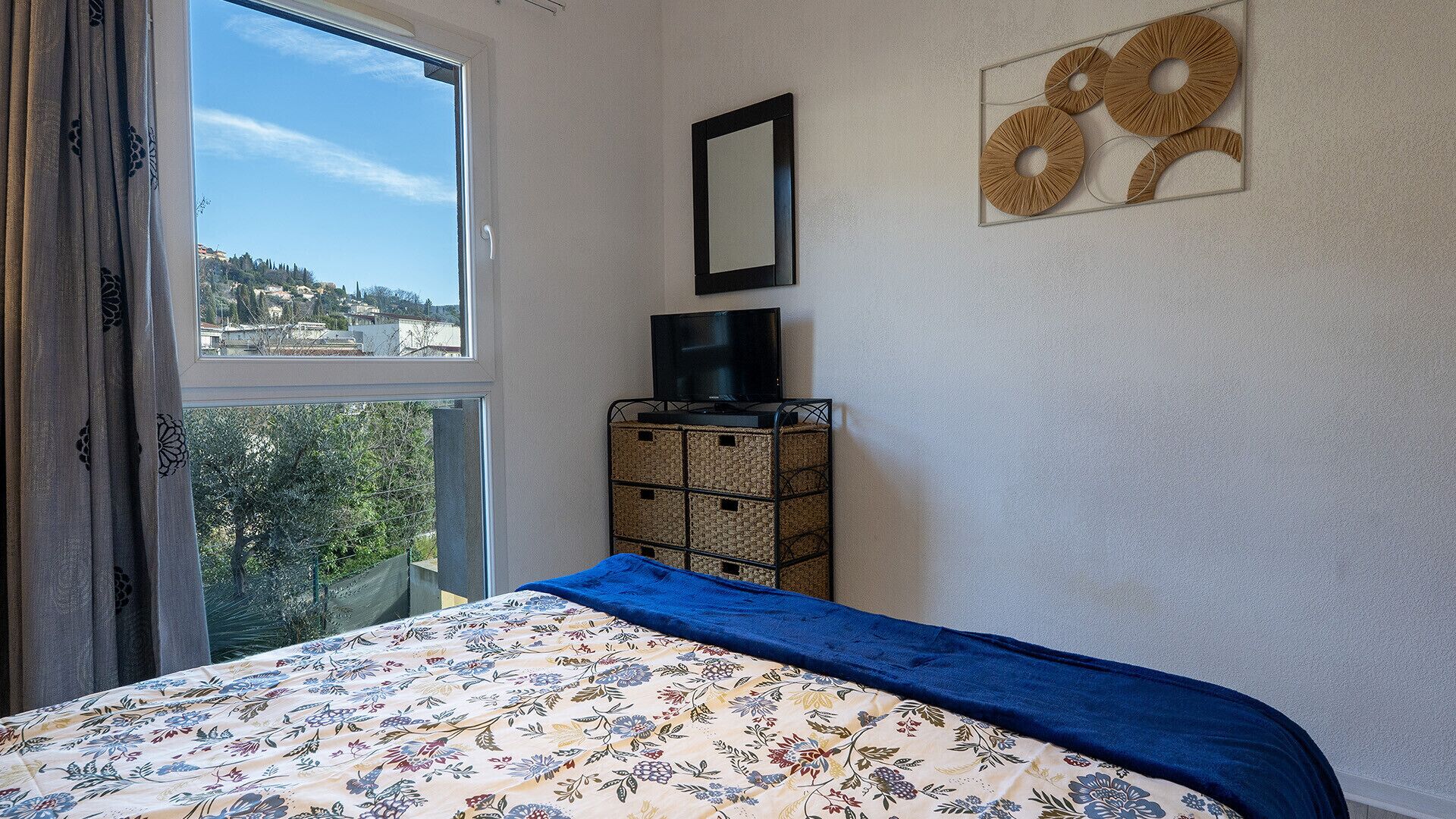 Ein Schlafzimmer mit Bett, Fernseher auf einem Schrank, einem Fenster mit Blick und einem Wandbild.