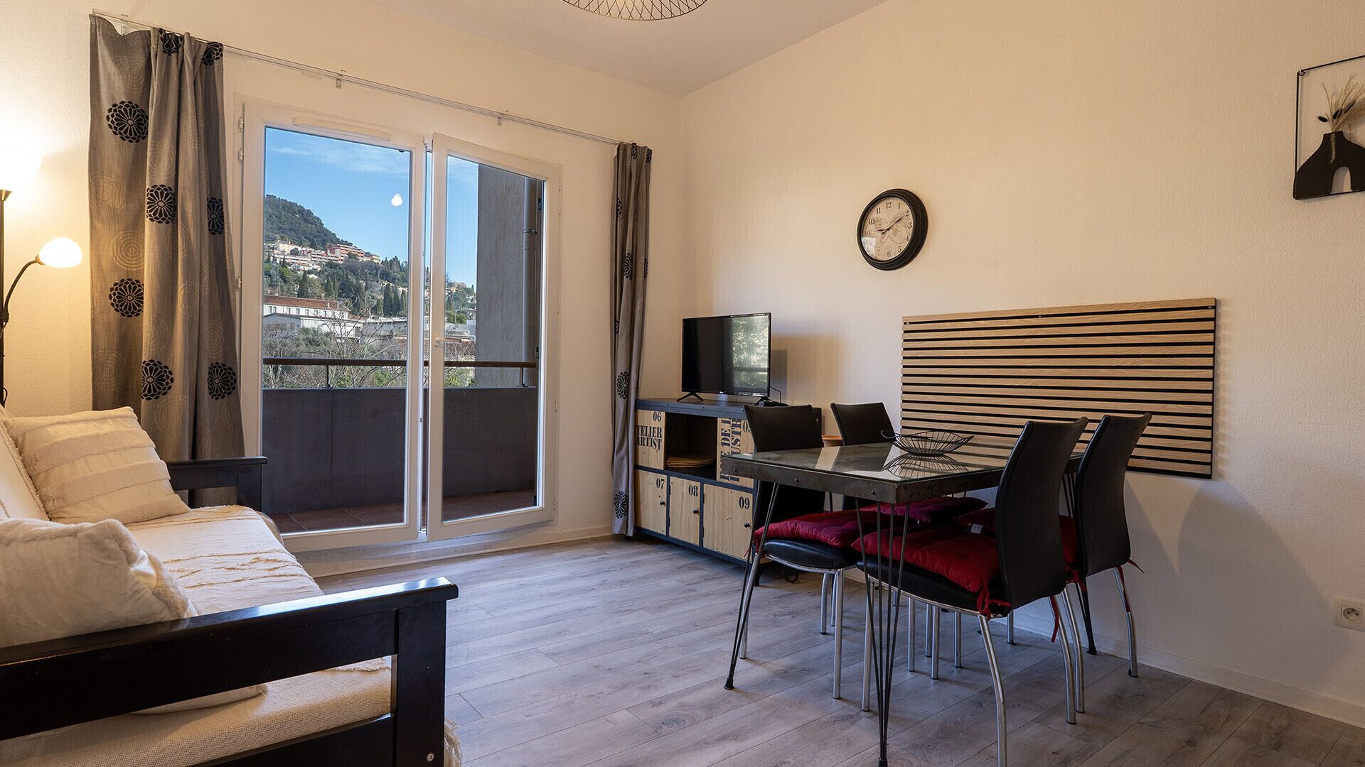 Une pièce comprenant un lit, une table à manger avec des chaises, un téléviseur et une horloge au mur.
