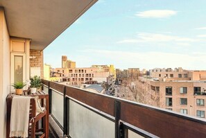 Ein Balkon mit Blick auf eine Stadtlandschaft, einem Holztisch und einem Blumentopf.