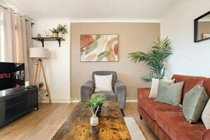 Ein Wohnzimmer mit einer Couch, einem Couchtisch, einem Fernseher, einer Lampe und einem Bild an der Wand.
