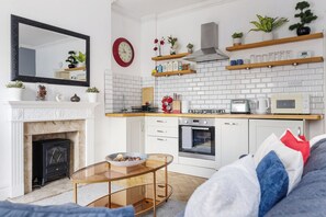 Eine moderne Küche mit weißen Schränken, einem Kamin, einem runden Spiegel und einem Essbereich mit einem Glastisch.
