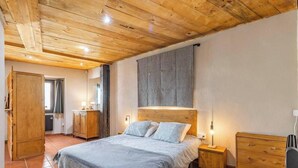 A bedroom with a wooden ceiling, a bed with a headboard, a nightstand, a dresser, and a wardrobe.