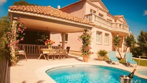 A poolside area with a covered seating area, lounge chairs, and a pool with a champagne bottle. - Villa Costa Dorada : Swimming pool, BBQ, 10 guests (Tarragona)