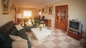 A living room with a checkered floor, a green sofa, a coffee table, a television, and framed pictures on the walls. - Villa Costa Dorada : Swimming pool, BBQ, 10 guests (Tarragona)