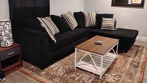 A modern living room with a black sectional sofa, striped pillows, a wooden coffee table, and a patterned rug. - Relaxing 1BR Near Downtown, TMC, NRG & Astros (Houston)