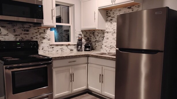 A kitchen with stainless steel appliances, white cabinetry, a window, and a patterned backsplash. - Relaxing 1BR Near Downtown, TMC, NRG & Astros (Houston)
