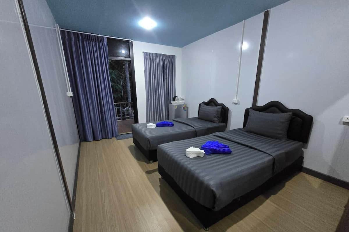 A hotel room with two beds, a small table, a chair, a window with curtains, and a door.