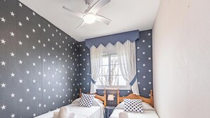 A room with two beds, a ceiling fan, a window with curtains, and star-patterned walls. - Family Oasis in Comarruga: Pool and Relaxation (El Vendrell)