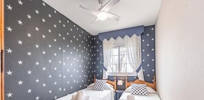 Ein Zimmer mit zwei Betten, einem Deckenventilator, einem Fenster mit Vorhängen und Wänden mit Sternenmuster.